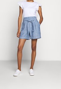 Džínové šortky s vysokým pasem a páskem na zavázání, doplněné bílým bavlněným tričkem s krajkovým lemem na rukávech. Bílé tenisky.