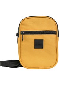 Žuta tkanina crossbody torbica s teksturiranom površinom, prednji zip džep, crni zatvarač i podesiva traka. Ima kvadratnu oznaku brenda.