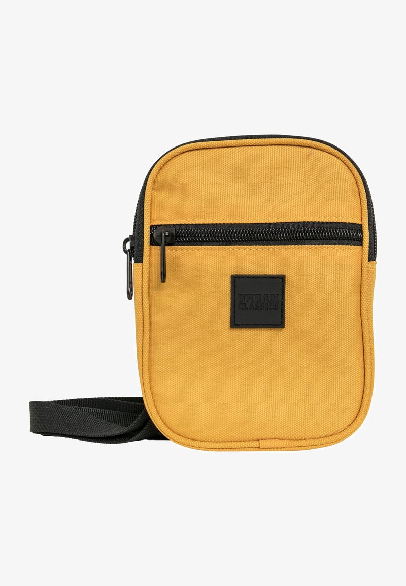 Rumena torba za čez ramo iz tkanine z teksturirano površino, sprednji žep na zadrgo, črna zadrga in nastavljiv trak. Ima kvadratno oznako blagovne znamke.