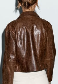 Brown leather jacket with a glossy texture, featuring a classic collar and tailored fit, showcasing stitching details along the seams.