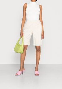 Bílý bezrukávový top, béžové upravené šortky, růžové sandály na podpatku a zelená kabelka. Hladké textury a kontrastní barvy.