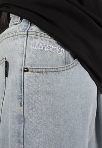 Light blue denim jeans with a textured finish, featuring embroidered "WASTED" logo on the back pocket and visible stitching details.