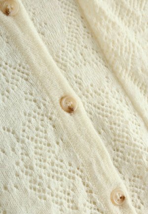 Gebreide cardigan in crèmekleur, met een textuurpatroon en kleine ronde beige knopen langs de voorkant. Zachte, lichte stof.