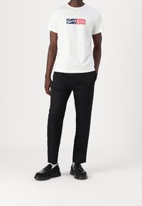 Biała koszulka z niebieskim i czerwonym nadrukiem "Tommy Jeans", zestawiona z czarnymi tapered spodniami i czarnymi chunky butami.