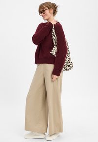 Burgundy, fluffy sweater, beige wide-leg trousers, and white sneakers. Carrying a leopard print tote bag, standing against a plain background.