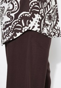 Tunique fluide avec un motif floral blanc et marron foncé, associée à un pantalon marron foncé uni. Le tissu semble léger avec une texture lisse.