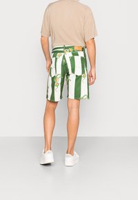 Zelenobílé pruhované kraťasy s motivem hadů a pomerančů. Vyrobené z denimu, mají zadní kapsy a koženou záplatu na pase.