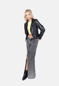 Chaqueta de cuero negra de motorista, top corto amarillo, falda maxi de mezclilla gris con abertura frontal, combinada con botas de tobillo negras con tacón.