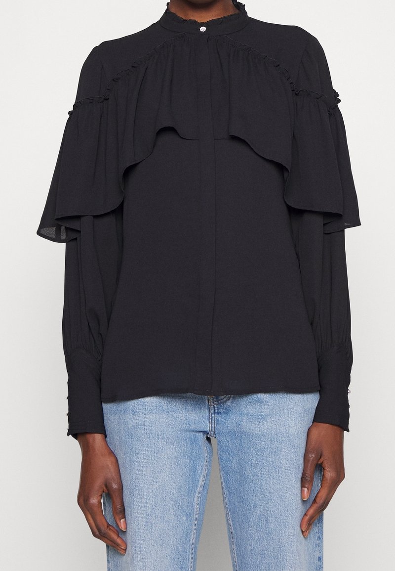 Schwarze Bluse mit geschichteten Rüschendetails, hohem Kragen und Knopfverschluss. Lange Ärmel mit gepufften Manschetten und aus einem glatten, leichten Stoff.