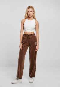 Brązowe spodnie z weluru o szerokiej nogawce, z elastycznym paskiem i sznurkiem. Połączone z białym krótkim topem i białymi trampkami.