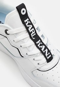 Fehér bőr sneaker, texturált fekete fűzőcímkével, ami "KARL KANI" felirattal rendelkezik, perforált részletekkel az orrán és világoskék akcentusokkal.
