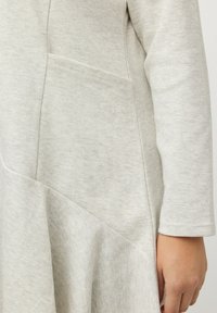 Vestido gris claro hecho de tela texturizada con un cuerpo ajustado y una falda en línea A, que presenta un bolsillo lateral y detalles de costura.