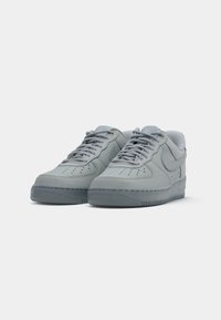 Svijetlosivi Nike Air Force 1 tenisice s vezicama, perforiranim prednjim dijelom i teksturiranim đonom na bijeloj pozadini.