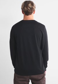 Chemise noire à manches longues en tissu doux. Elle présente un col rond et des détails de couture minimalistes sur les épaules. Design uni, sans motifs.
