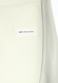 Tejido blanco con una textura suave, que presenta una etiqueta que dice "MWMN x mod wave movement" en texto negro, cosida en una costura lateral.