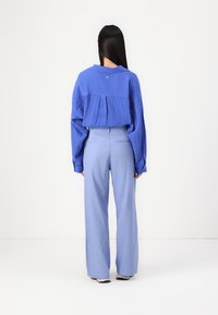 Blauwe textuur oversized blouse met een rugplooien, gecombineerd met lichtblauwe wijdvallende broek, met een hoge taille en knoopdetails.