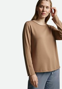 Braunes Langarmoberteil mit Rundhalsausschnitt, strukturiertem Stoff und lockerer Passform. Kombiniert mit hellblauen, schimmernden Hosen.