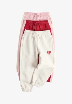 Tre sammenlagte joggingbukser i creme, rød og pink, med elastiske linninger og et lille rødt smilende hjerte på cremeparret.