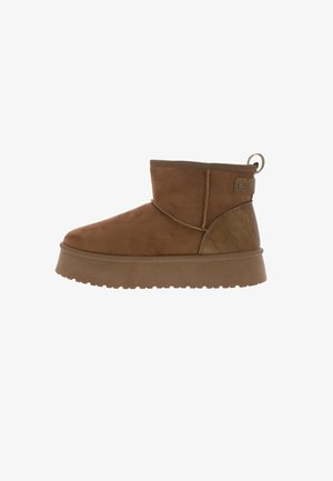 Stivaletto in suede marrone con suola piatta in gomma, cucitura laterale e linguetta sul retro per facilitarne l'indossamento. Texture liscia con accenti minimi.
