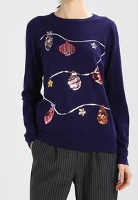 Jersey navy con un diseño embellecido de adornos coloridos y estrellas. La tela suave y los puños acanalados mejoran la textura y la comodidad.