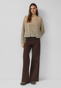 Feller beige gestrickter Pullover mit hohem Kragen, kombiniert mit dunkelbraunen Schlaghosen und schwarzen Gummisohlen-Stiefeletten.