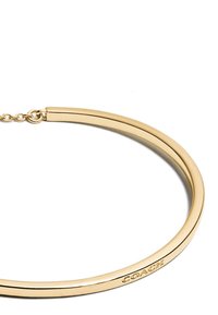 Gold bangle bracelet with a smooth, rounded shape and polished finish. Features a subtle engraved logo on the edge. Adjustable clasp.