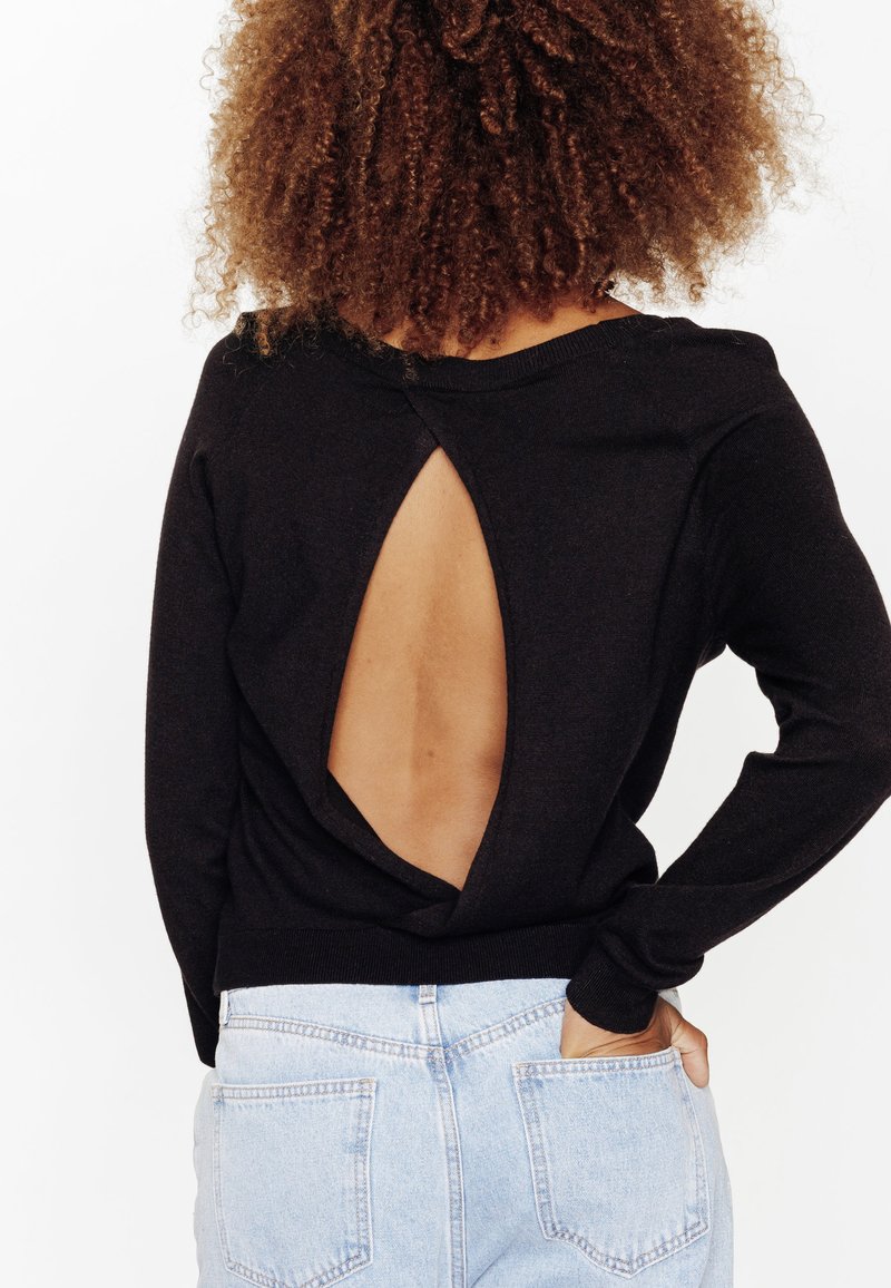 Maglione nero con scollatura profonda sulla schiena, collo a coste e maniche lunghe, abbinato a jeans a vita alta blu chiaro.