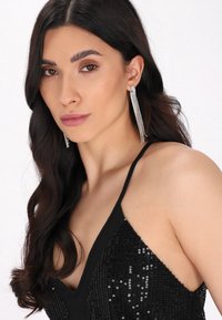 Černé flitrové šaty s hlubokým výstřihem do V a tenkými ramínky. Dlouhé stříbrné náušnice s více prameny třpytivých rhinestones.