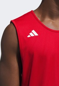 Rød atletisk tanktop med en åndbar mesh-struktur, udstyret med hvide Adidas-logo detaljer på venstre skulder og halsudskæring.