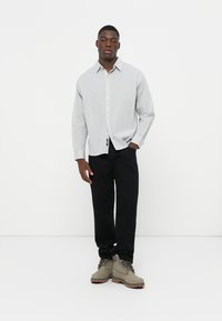 Striped button-up shirt in light gray and white, paired with black pants and beige boots. The shirt features a single pocket and long sleeves.