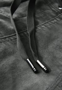 Grijze stof met twee bijpassende trekkoorden; elk heeft een gestructureerd oppervlak en metalen tips. Glad textuur met subtiele stikseldetails.