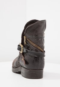 Zwart leren enkellaarsje met een geperst bloemenpatroon, een ritssluiting aan de zijkant en een riem met gespdetail. Plat hakontwerp.