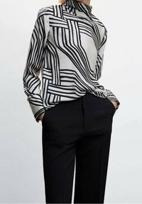 Blouse à motifs noirs et blancs avec un col montant, des manches longues et une coupe ample, assortie à un pantalon noir, mettant l'accent sur des lignes géométriques.