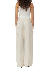 Beige wijde cargo broek van zacht materiaal met zij- en achterzakken, met een ontspannen pasvorm en een gladde, glanzende textuur.