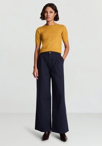 Mustard short-sleeve sweater paired with high-waisted, wide-leg navy trousers and dark brown ankle boots. Smooth texture throughout.