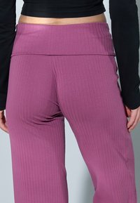 Leggings violets côtelés avec une large ceinture haute. Le tissu semble doux avec une texture verticale. Un haut noir à manches longues est partiellement visible.