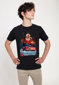 Černé tričko s barevnou grafikou Santa Clause a kamionu Coca-Cola, s bílým textem "Svátky se blíží!"