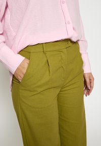 Olivno zeleni hlače z ravnim sprednjim delom in stranskimi žepi, ujemajoče se s svetlo rožnatim, teksturiranim srajco z gumbi, ki ponuja sproščen kroj.