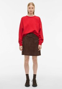 Röd oversized sweatshirt, brun mockaskjorta med bälte och bruna skor. Slät textur, rak passform och fickor på kjolen.