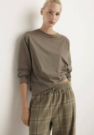 Bruine lange mouwtop gecombineerd met geruite, beige en groene broek met een elastische taille en trekkoord. De stof lijkt zacht en ontspannen.