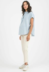 Camicia a righe blu chiaro con maniche corte, davanti con bottoni e vestibilità ampia, abbinata a pantaloni crema e sneakers bianche con accenti verdi.