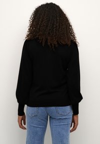 Czarny sweter z balonowymi rękawami i ribbovaną wykończeniem, zestawiony z jasnoniebieskimi dżinsami. Miękka tekstura, minimalistyczny design, dopasowany krój.
