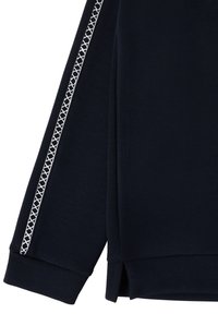 Manche longue bleu marine avec une bande à motifs géométriques blancs courant le long du bras, poignets côtelés et fentes latérales à l'ourlet.