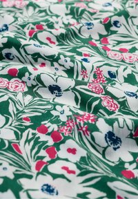 Floral fabric featuring a green background with white flowers, pink accents, and blue details. Soft texture with a delicate pattern.