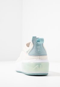 Nike Air-sneaker med vit sula, ljusblå bakledd och blekgrön genomskinlig luftkudde, visad bakifrån på vit bakgrund.