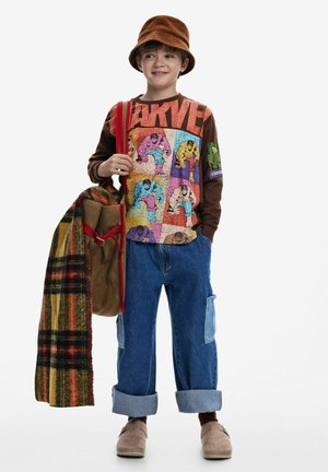 Brown long-sleeve shirt with multicolored superhero graphics, blue baggy jeans with rolled cuffs, tan shoes, and a brown corduroy hat. Red strap bag.