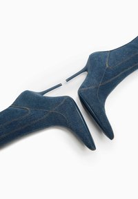 Džínové kotníkové boty s špičatými špičkami, vysokými stiletto podpatky a kontrastním žlutým prošíváním. Hladký povrch s pevnou konstrukcí.