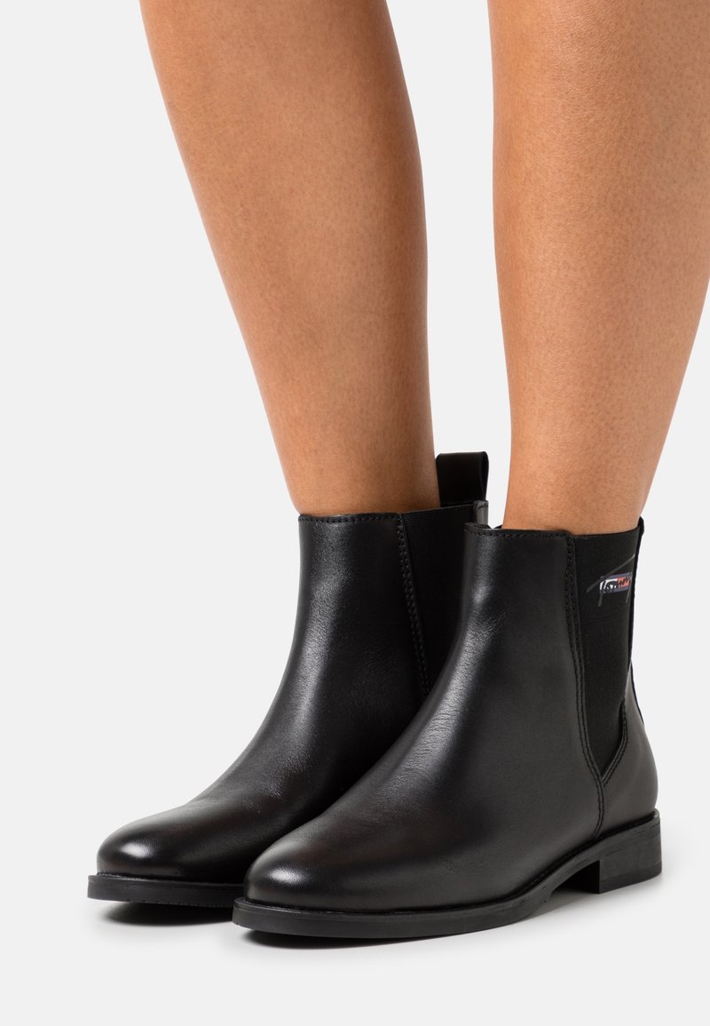 Bottes noires pour chevilles en cuir lisse, dotées de panneaux élastiques sur les côtés, d'un talon bloc bas et d'une languette à l'arrière pour un enfilage facile.