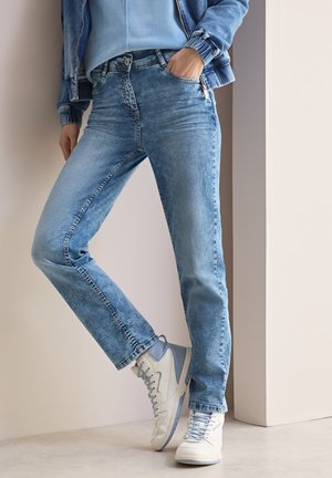 Vaqueros de denim azul claro con corte slim, que cuentan con cinco bolsillos y un detalle de cremallera. Combinados con zapatillas altas de color azul claro y blanco.