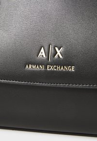 Portofel din piele neagră cu logo embossat "A/X" și "ARMANI EXCHANGE" în aur, cu detalii vizibile de cusătură și o textură netedă.